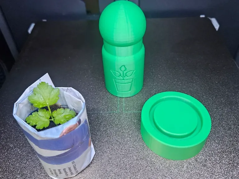 Green two-part paper pot maker beside a newspaper seed pot holding a small plant